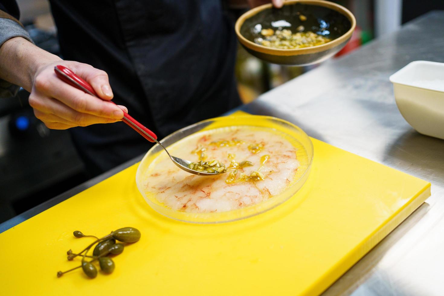 Cuisinier anonyme répandant de la sauce aux pignons de pin sur une assiette de carpaccio de crevettes photo