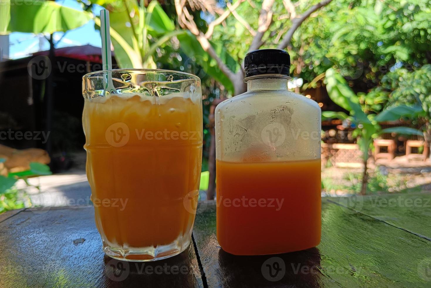 jus d'orange frais dans le bocal en verre et la bouteille, jus de fruits pour se rafraîchir, arrière-plan flou de bananier photo