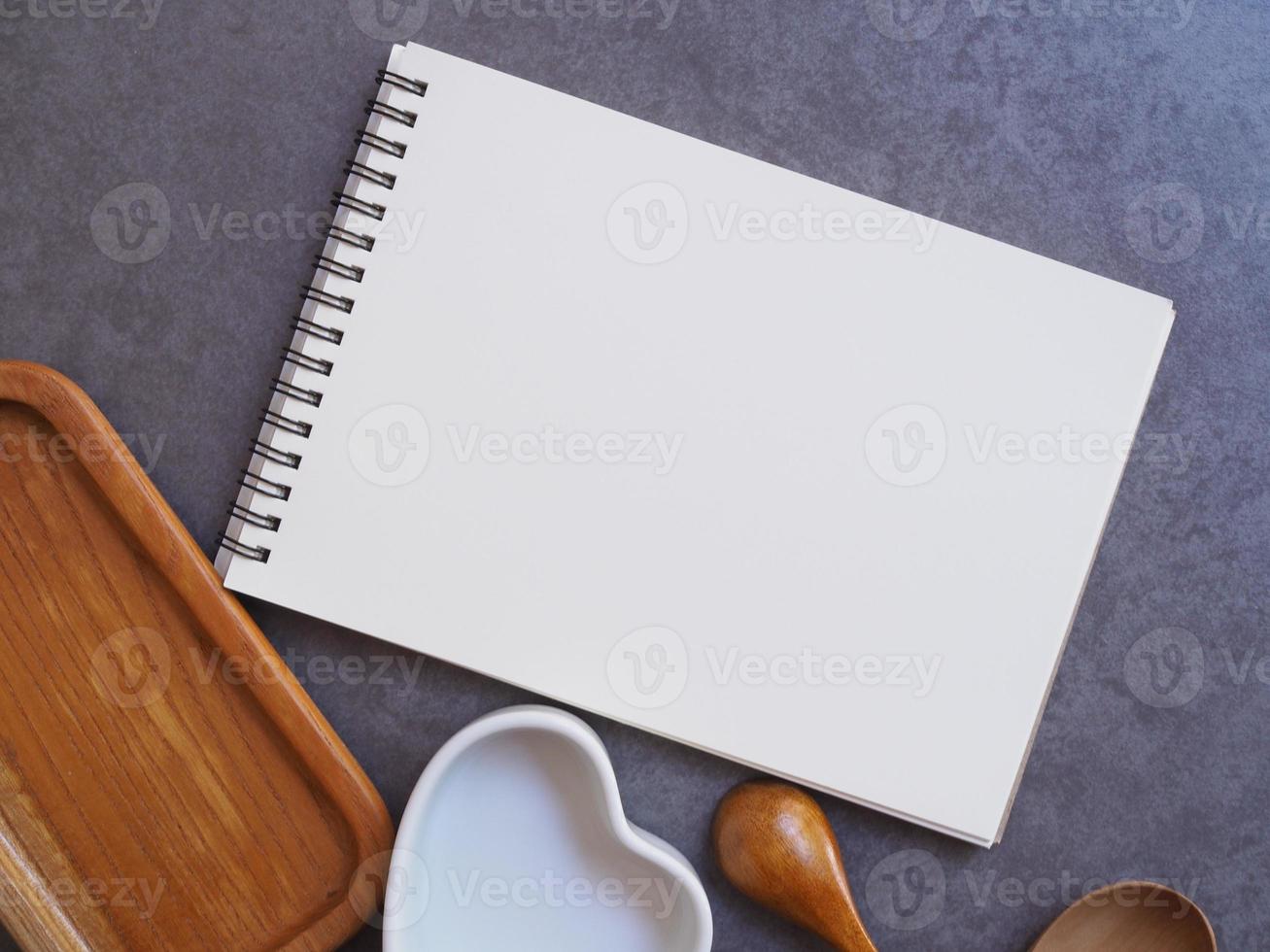 livret de recettes, cuillère, bol blanc et plateau en bois sur fond de ciment. photo