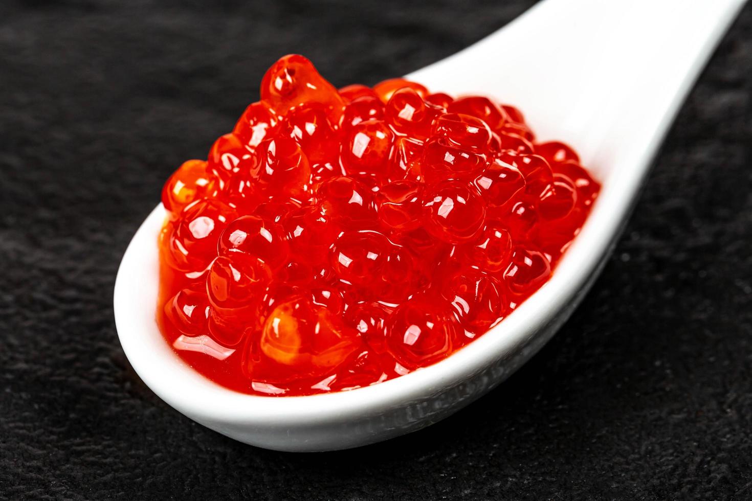 gros plan de caviar rouge dans une cuillère blanche sur fond noir photo