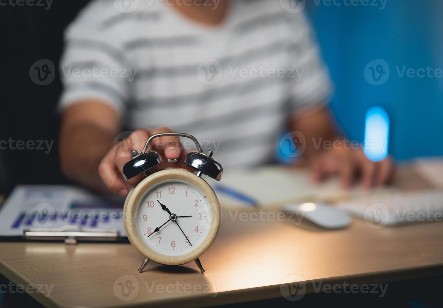 mise au point sélective du réveil et de l'homme indépendant appuyant sur le bouton du réveil tout en travaillant à la maison. homme d'affaires travaillant des heures supplémentaires la nuit à la maison. photo