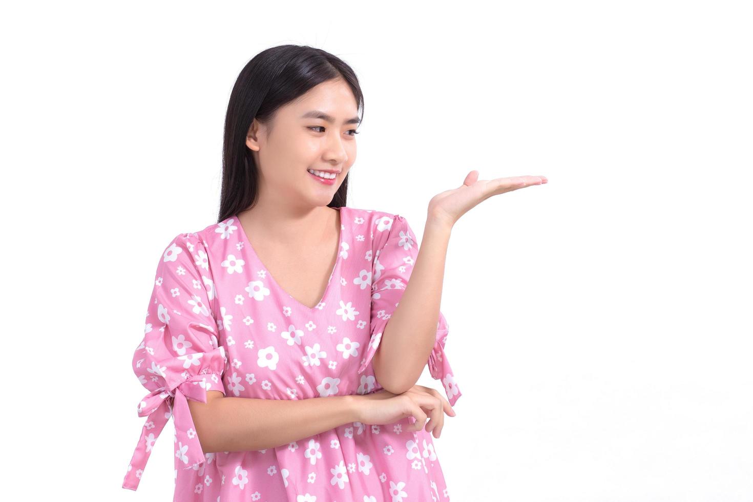 une femme asiatique en robe rose montre sa main pour présenter quelque chose sur fond blanc. photo