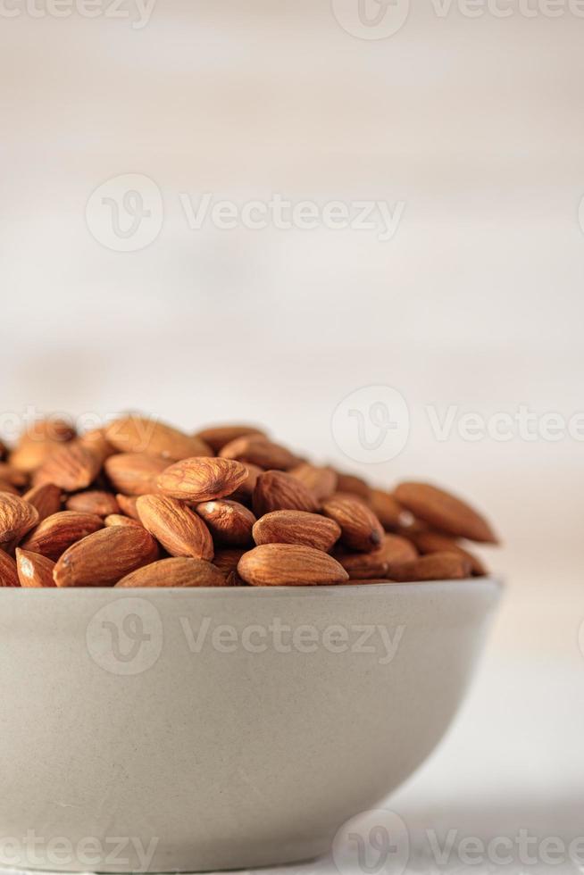 amandes dans un bol en céramique sur une table en bois blanc.matière première de régime biologique photo