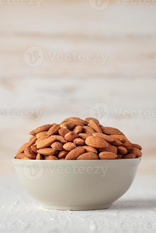 amandes dans un bol en céramique sur une table en bois blanc.matière première de régime biologique photo