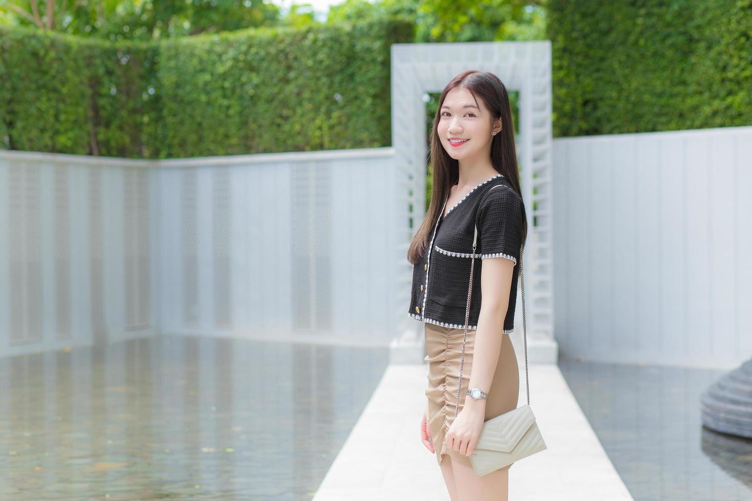 une jeune travailleuse asiatique aux cheveux longs dans une chemise noire sourit joyeusement en se promenant dans le parc extérieur pour aller travailler au bureau. photo