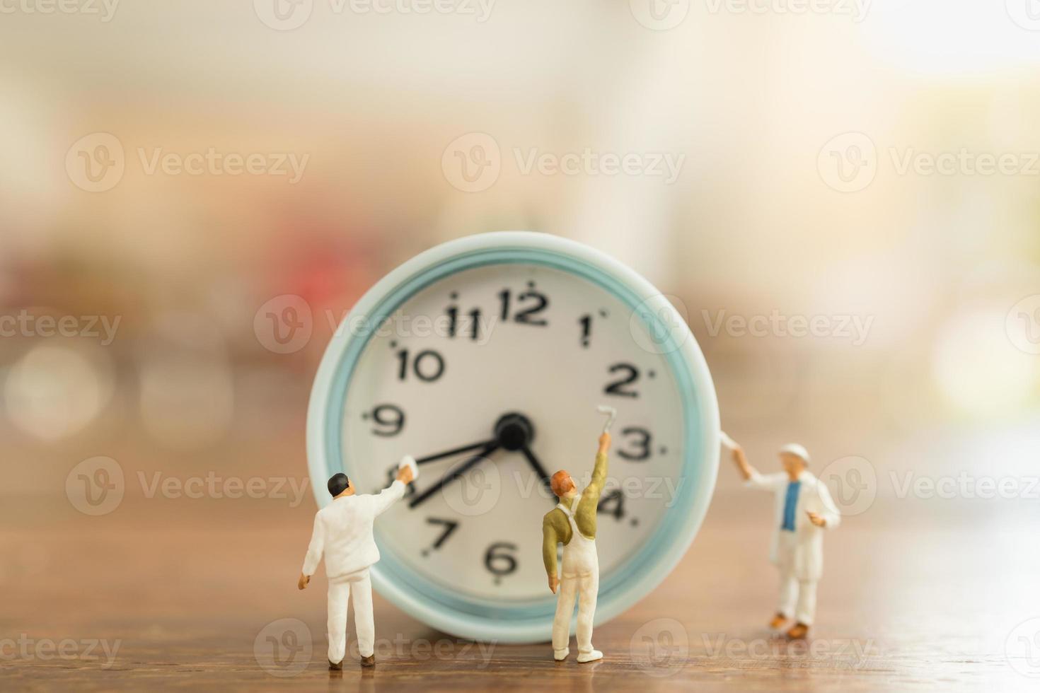 notion de gestion du temps. gros plan d'un groupe de figurines de travailleurs miniatures nettoyer et peindre une horloge ronde vintage sur une table en bois. photo