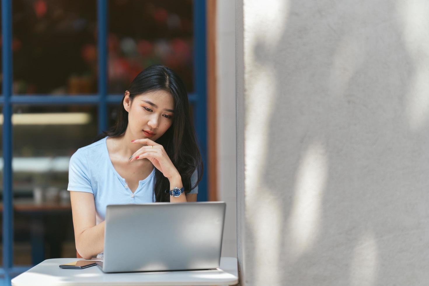 portrait d'une belle femme asiatique assise à l'extérieur au café-restaurant pendant l'été, à l'aide d'un ordinateur portable et d'un smartphone à technologie sans fil intelligente, pause-café relaxante au café-restaurant. photo