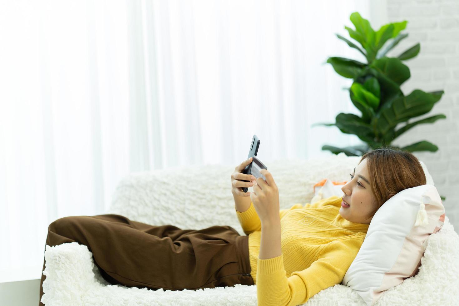 une femme asiatique en vêtements décontractés est heureuse et joyeuse tout en communiquant avec son smartphone et en travaillant à la maison. photo