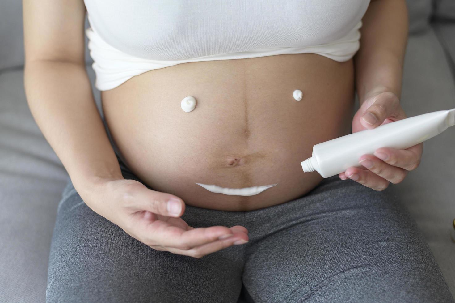 jeune femme enceinte appliquant une crème hydratante sur le ventre, les soins de santé et les soins de grossesse photo