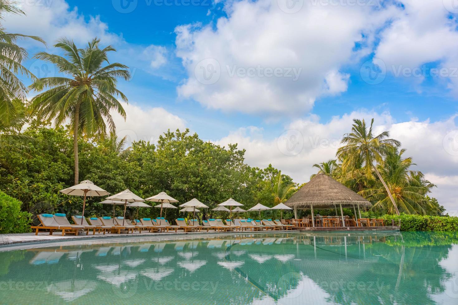 paysage de tourisme de plein air. station balnéaire luxueuse avec piscine et chaises longues ou transats sous des parasols avec palmiers et ciel bleu. concept de fond de voyage et de vacances d'été photo