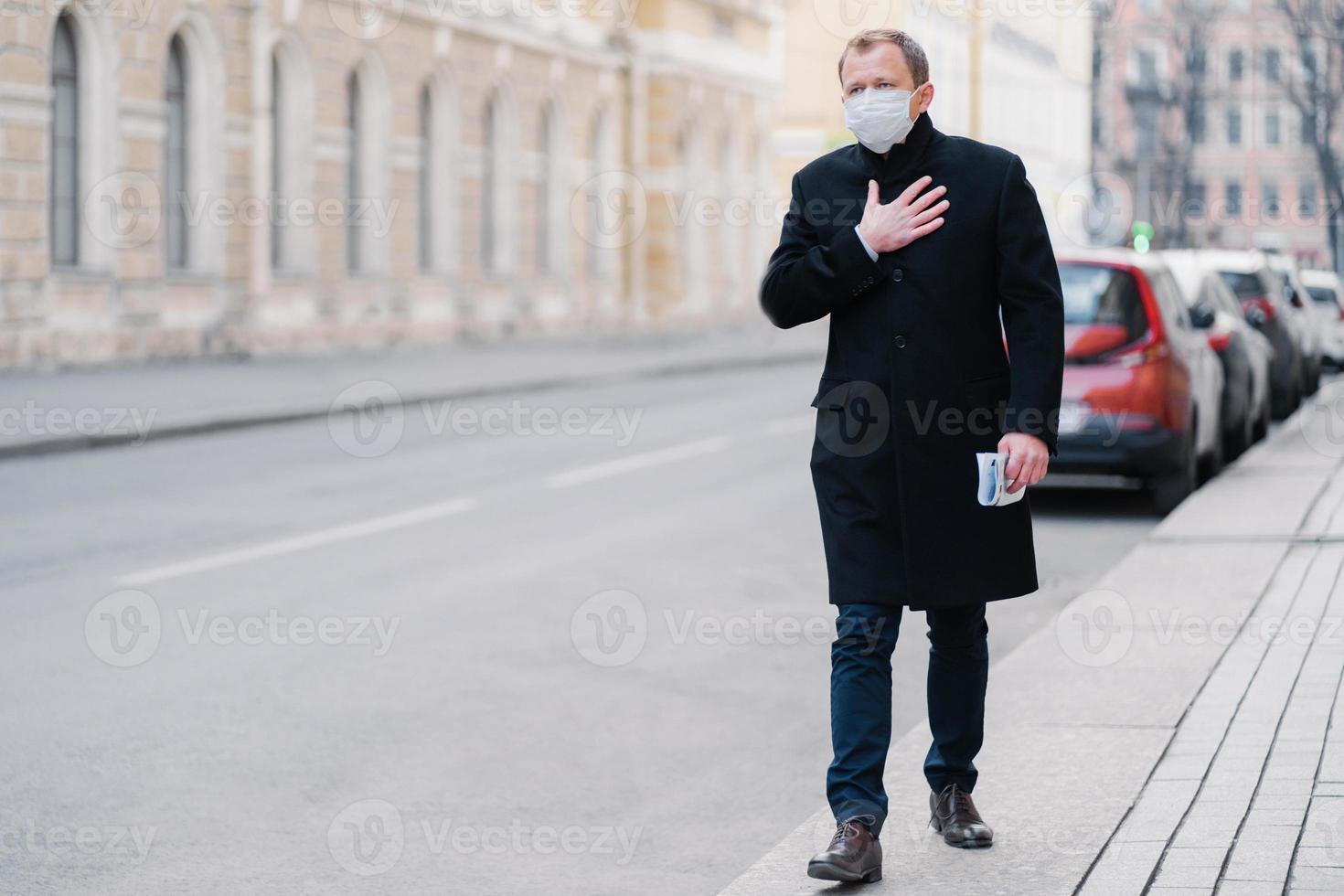 tir extérieur de l'homme va travailler, a des problèmes de respiration, garde la main sur la poitrine, porte un masque médical, préoccupé par la maladie pandémique, pose à l'extérieur. attaque de virus, concept de problème de santé photo