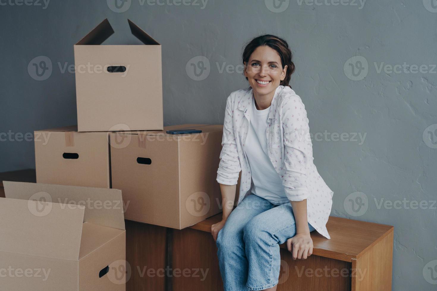 heureuse adolescente se déplace. une dame hispanique est assise sur des boîtes dans un nouvel appartement et sourit. photo