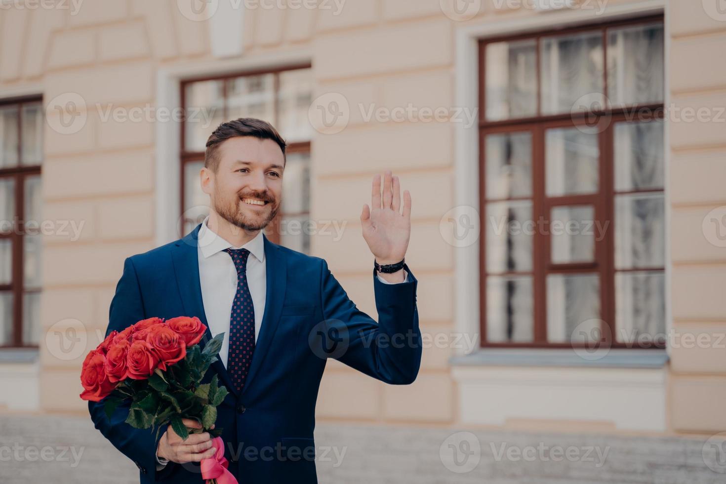 beau jeune homme en costume avec bouquet de roses saluant son partenaire commercial avec bouquet de roses rouges photo