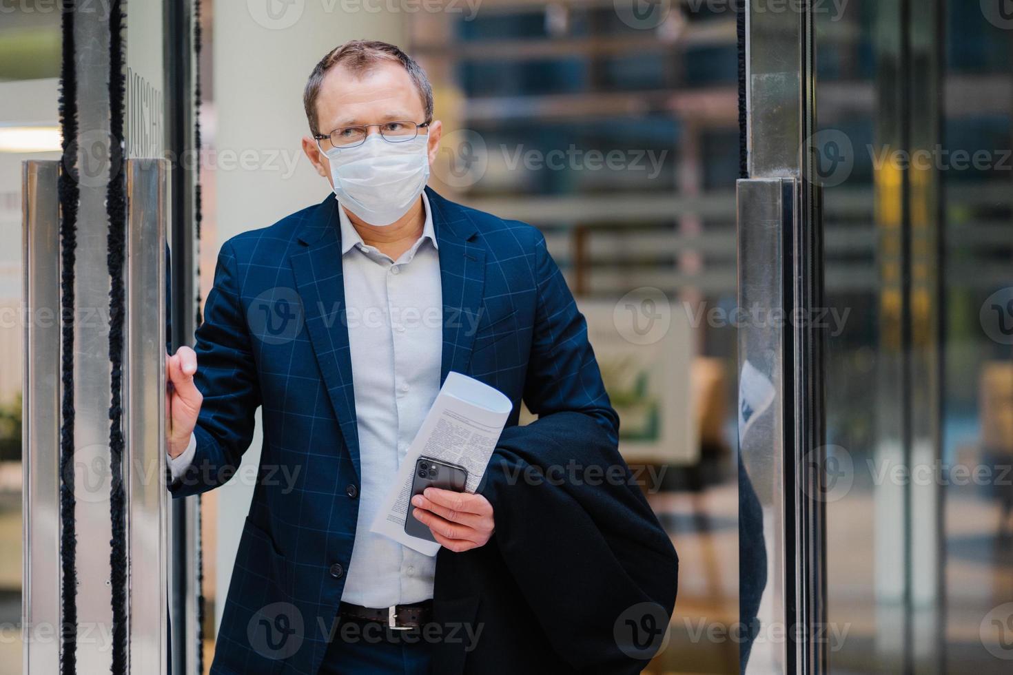 covid-19, concept de coronavirus pandémique. l'employé de bureau quitte le travail, porte un masque médical pour la propagation des maladies infectieuses, habillé formellement, tient un journal et un smartphone. notion de santé et de sécurité photo