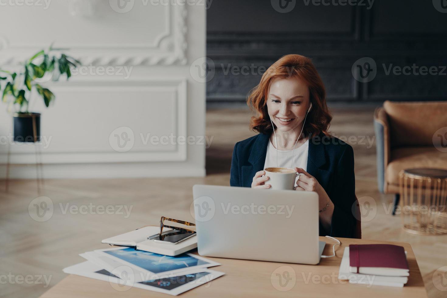 heureuse femme aux cheveux roux a un travail à distance, communique par chat vidéo avec des collègues, discute d'idées de projet, profite d'une conférence en ligne utilise un ordinateur portable moderne et des accessoires satisfaits d'une conversation amicale photo