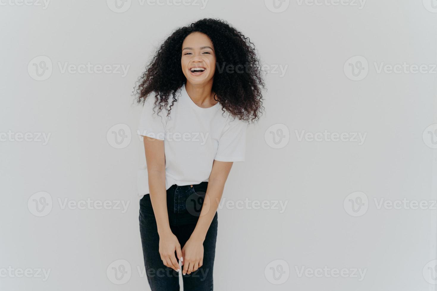 prise de vue en studio d'une joyeuse femme afro-américaine rit joyeusement, vêtue de vêtements décontractés, se sent bien, pose sur fond blanc avec un espace vide pour votre contenu publicitaire, se sent énergisée photo