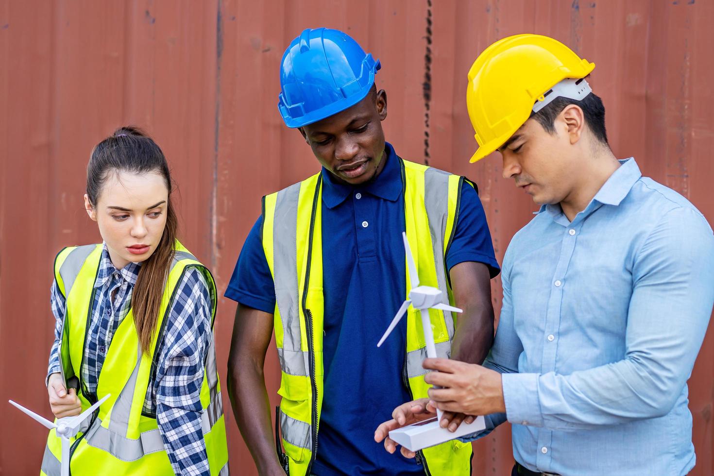 trois architectes homme et femme travaillant sur un projet de construction. jeunes collègues masculins et féminins debout sur un lieu de travail amical discutant sur un moulin à vent modèle photo