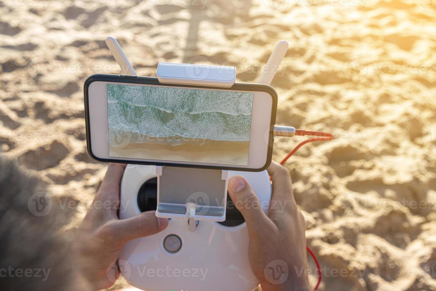 gros plan des mains de l'homme tenant le contrôleur pour un drone avec téléphone. photo recadrée de mains de jeune homme tenant la télécommande d'un drone volant à la plage