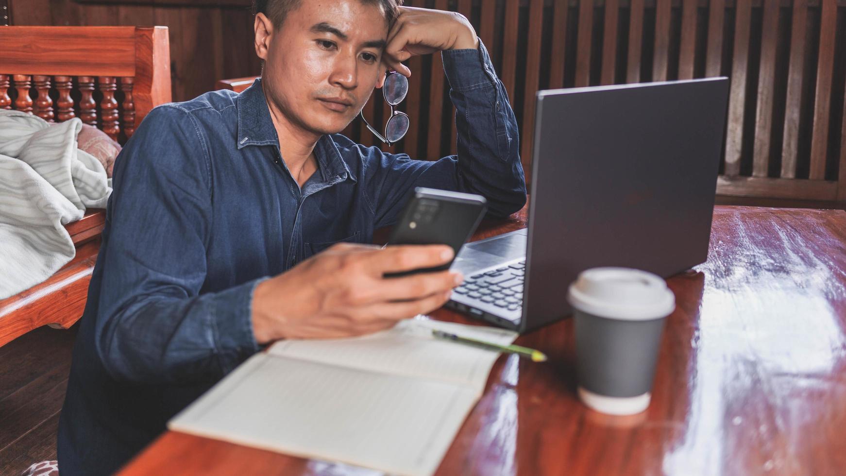 jeune homme travaillant à domicile à l'aide d'un téléphone intelligent et d'un ordinateur portable. photo