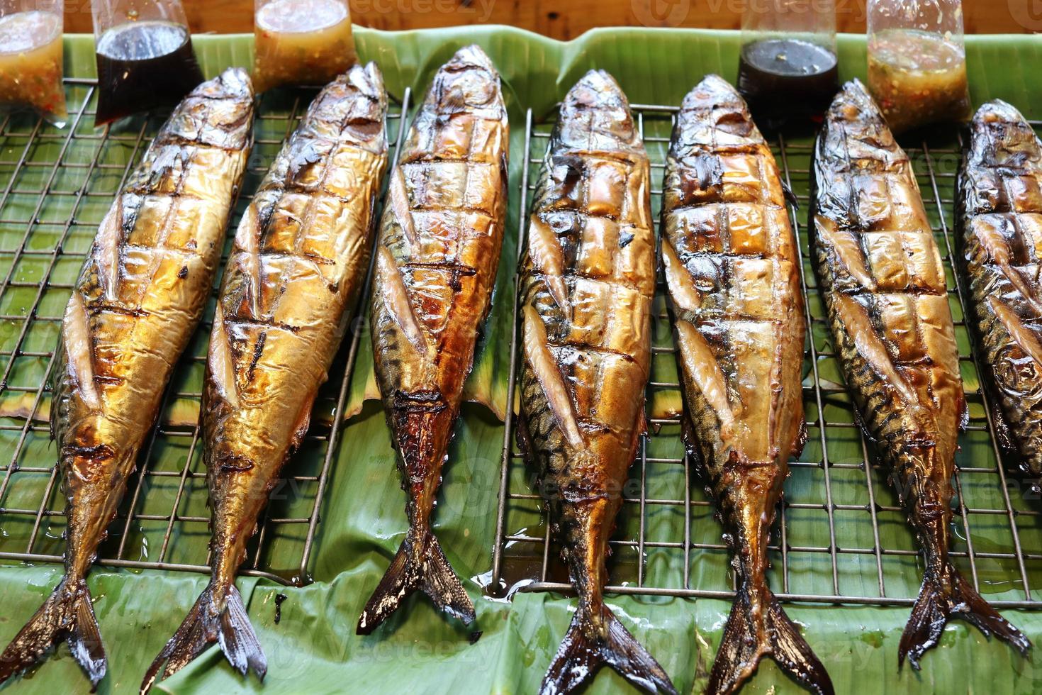 les poissons saba grillés sont sur une grille en acier inoxydable au-dessus des feuilles de bananier à vendre avec sauce, thaïlande. photo