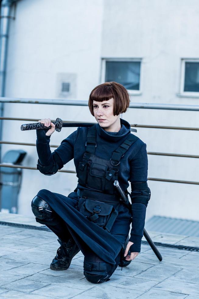 portrait d'une jeune femme rousse avec une épée japonaise vêtue d'un costume cyberpunk futuriste debout sur le toit. photo