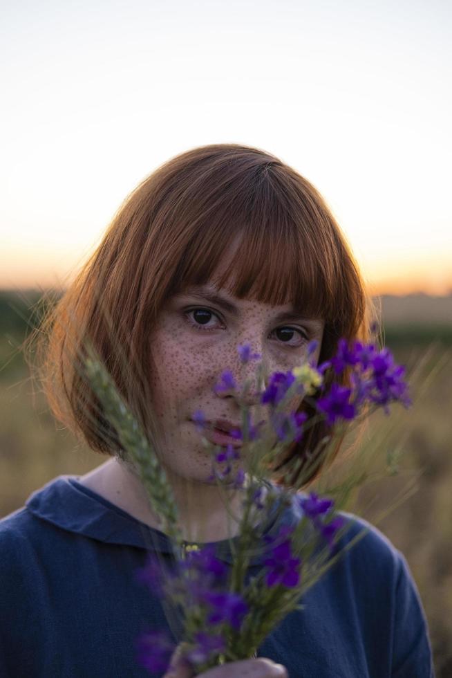 jeune femme rousse avec des taches de rousseur en robe vintage faite à la main à pied dans les champs de fleurs photo