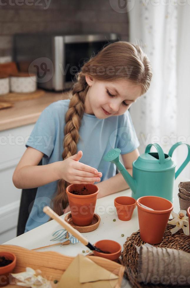 petite fille assise à la table à la maison, semant des graines dans des pots de fleurs. photo