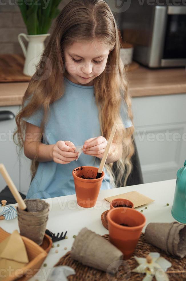 petite fille assise à la table à la maison, semant des graines dans des pots de fleurs. photo