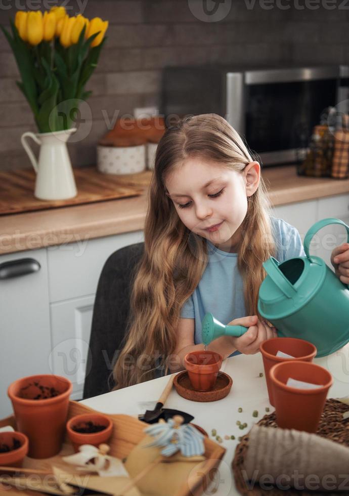 petite fille assise à la table à la maison, semant des graines dans des pots de fleurs. photo