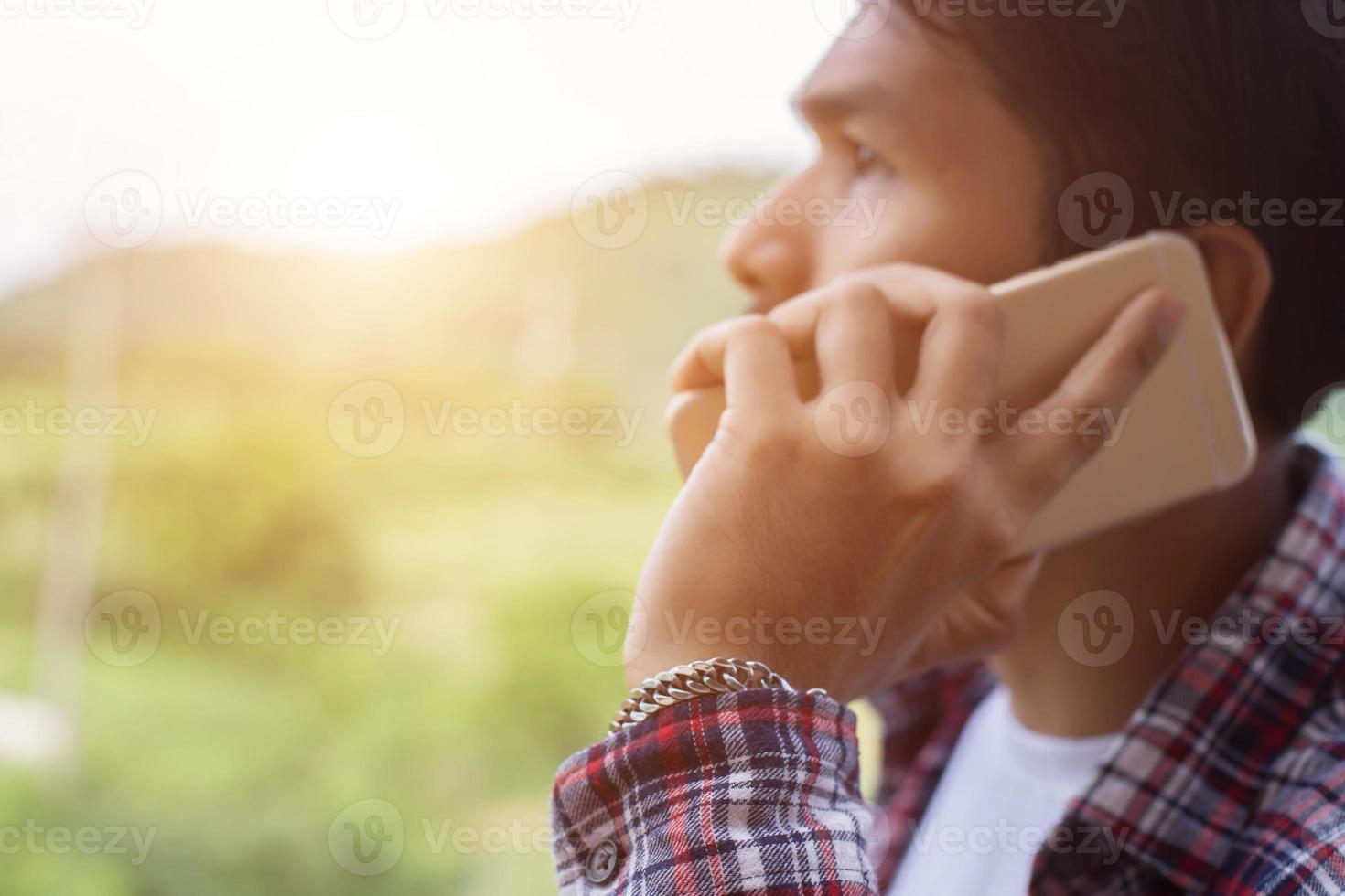 jeune homme barbu hipster parlant au téléphone, souriant, à l'extérieur de la vue sur la montagne. photo