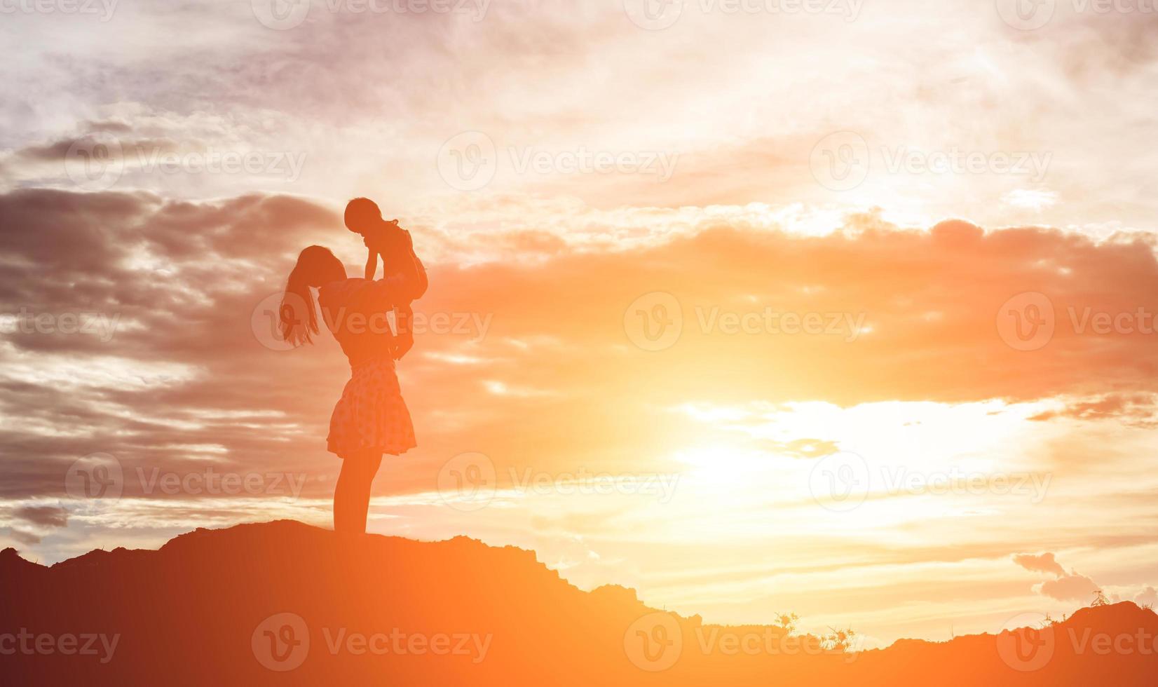 une silhouette d'une jeune fille heureuse dans les bras de sa mère aimante pour un câlin, devant le coucher de soleil dans le ciel un jour d'été. photo