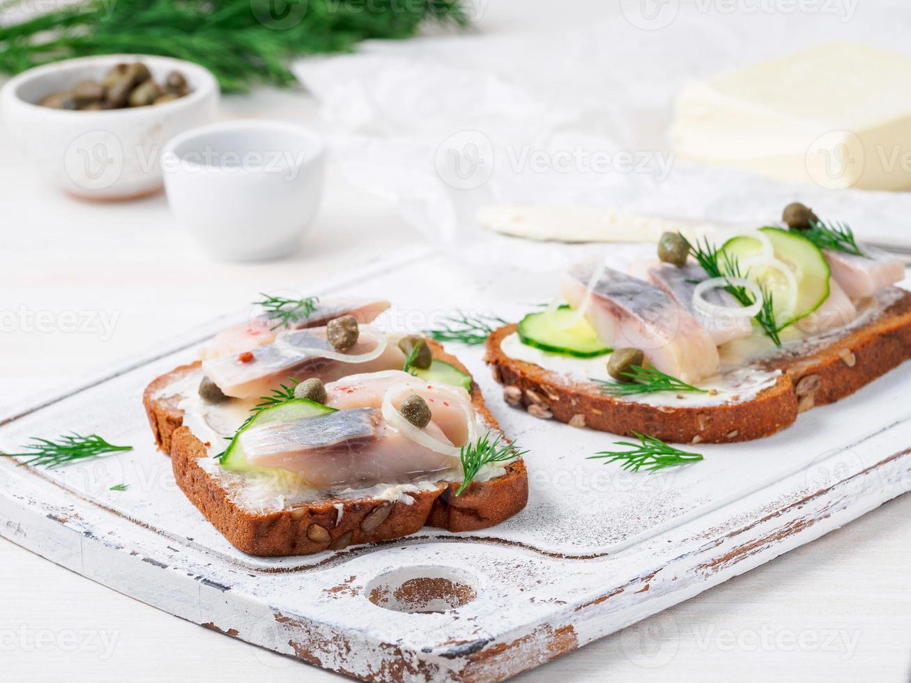 hareng smorrebrod - sandwichs danois traditionnels. pain de seigle noir avec hareng sur planche de bois blanc, vue latérale photo
