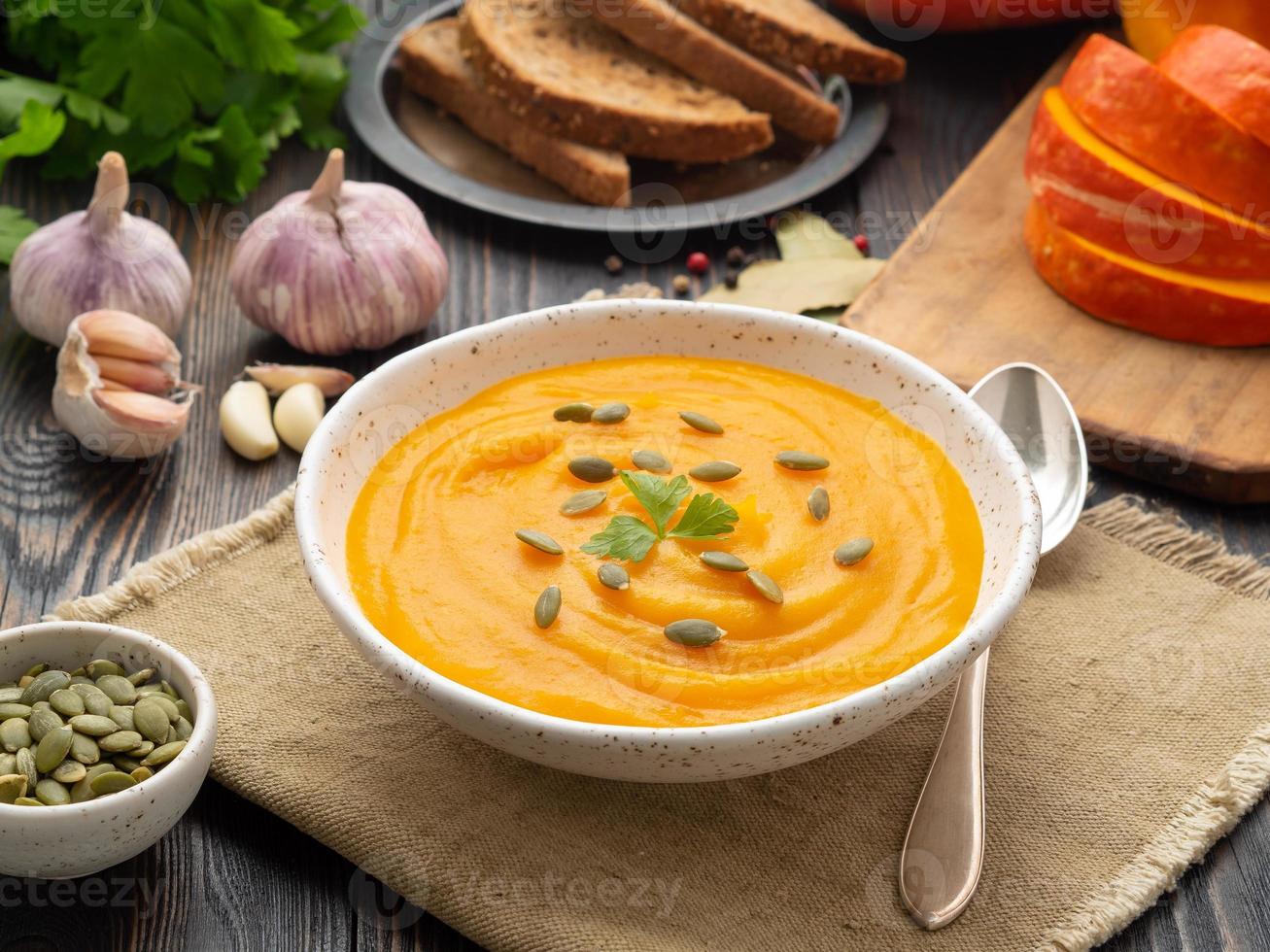 soupe de citrouille écrasée dans une assiette blanche, graines de citrouille, pain, ail sur fond de bois foncé photo