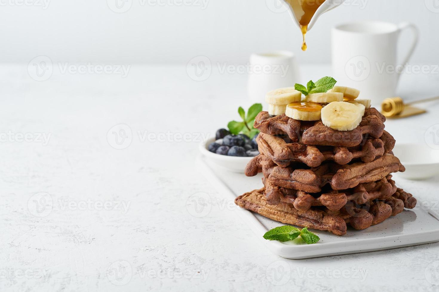 gaufres à la banane au chocolat avec sirop d'érable sur tableau blanc, espace copie, vue latérale. brunch sucré, goutte de sirop d'érable. photo