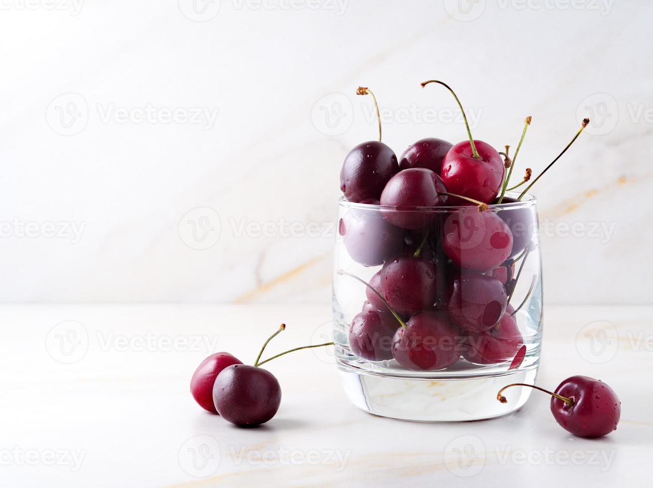 cerises douces rouges foncées en verre sur une table blanche en pierre, vue latérale, espace pour copie photo