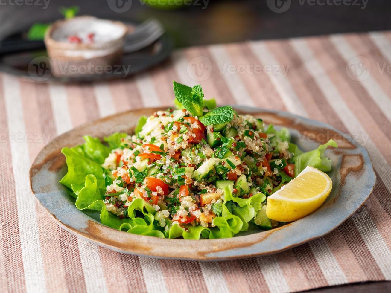 salade de taboulé au quinoa. cuisine orientale avec mélange de légumes, régime végétalien. vue de côté, serviette en lin, vieille assiette photo