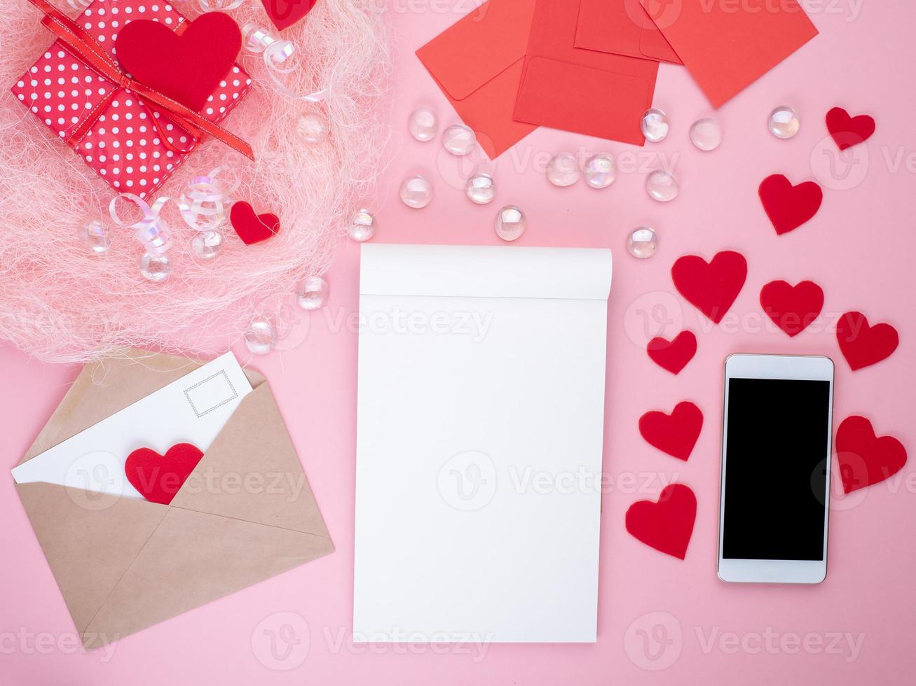 cadeau dans une boîte cadeau rouge avec noeud, bloc-notes, téléphone intelligent, enveloppe, carte, coeur rouge, fond rose, plat, espace pour copie photo