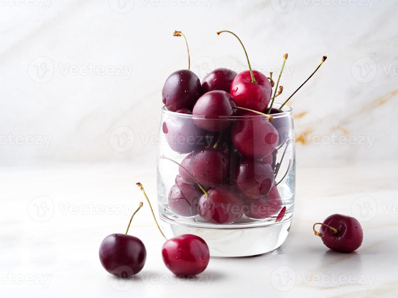 cerises douces rouges foncées en verre sur une table blanche en pierre, vue latérale, espace pour copie photo