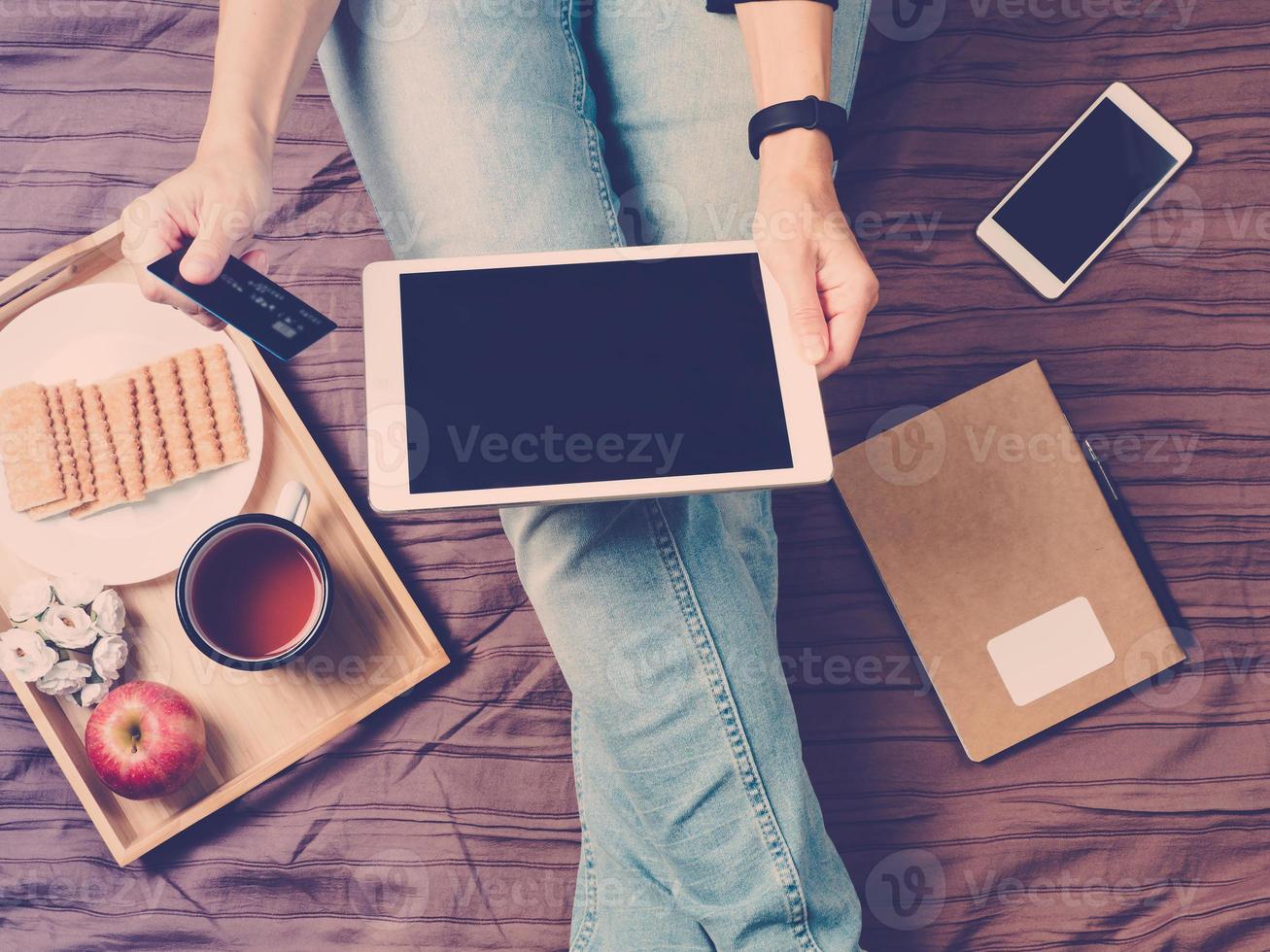 une femme assise sur son lit, buvant du thé et regardant une tablette, paie pour faire du shopping, faire du shopping en ligne photo