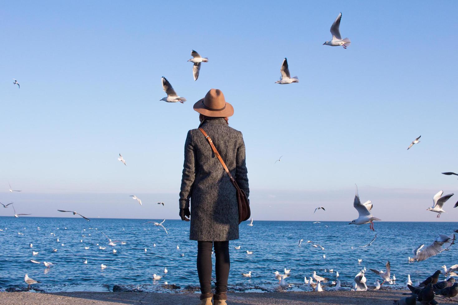 jeune femme au chapeau debout sur la plage d'automne n journée ensoleillée et regardant les mouettes photo