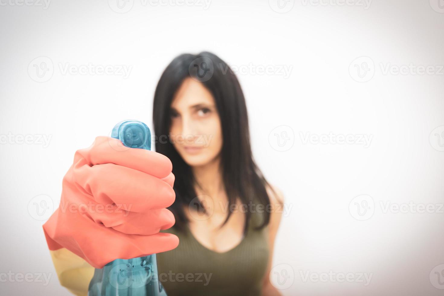 jolie femme caucasienne dans des gants pointe un flacon pulvérisateur de solvant bleu droit isolé sur fond blanc gris. femme de ménage et concept de maison de nettoyage. noir et blanc photo