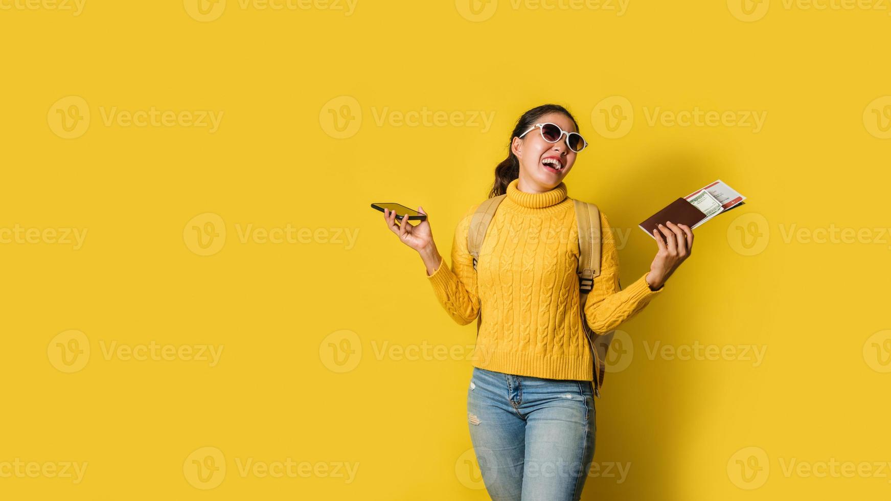 femme voyageuse avec valise, tenant un passeport et un billet dans la main et des téléphones portables sur fond jaune. concept de voyage autour du monde. sac à dos de voyage photo