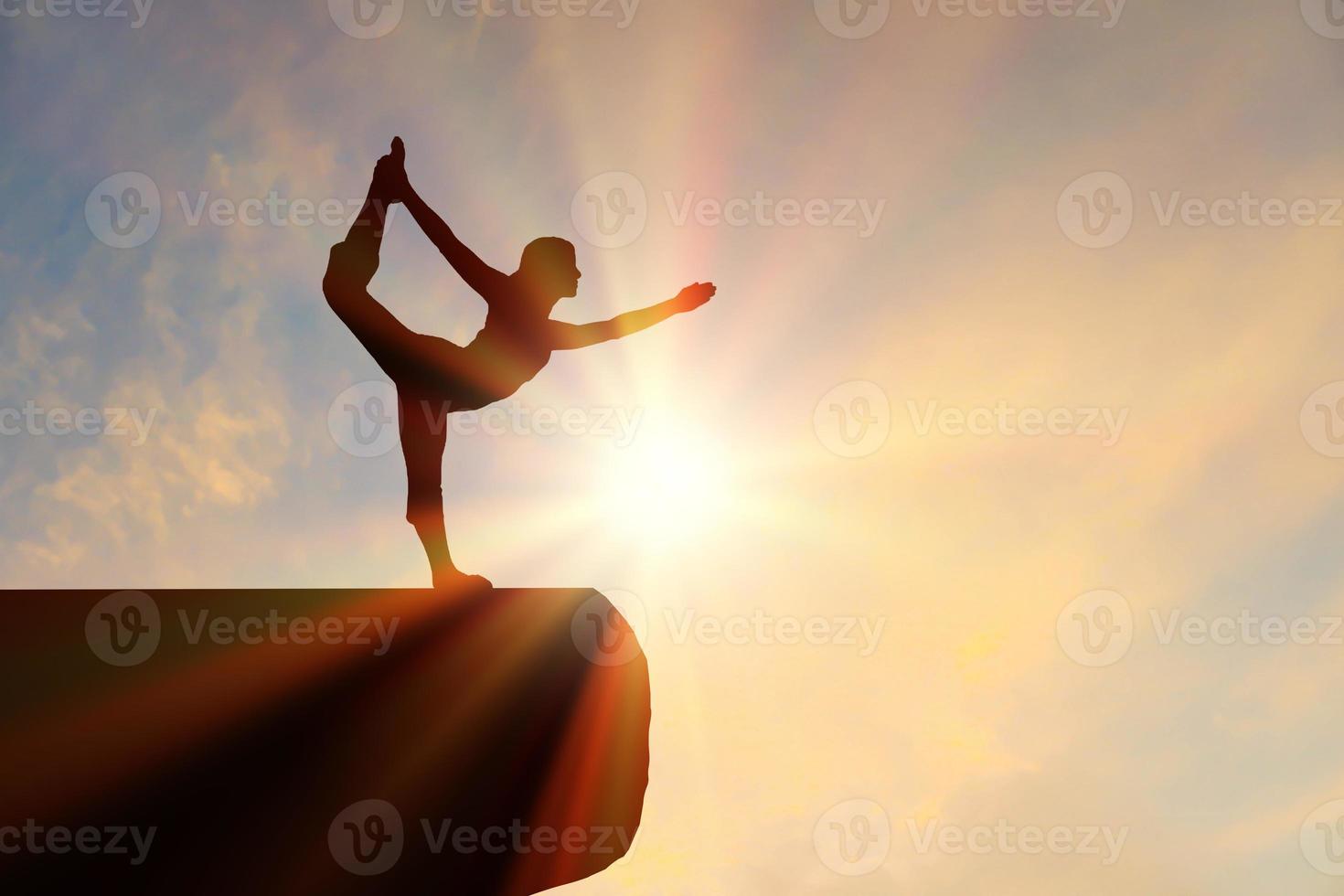 les femmes de silhouette de portrait font du yoga sur la pierre de silhouette avec un coucher de soleil orange calme. photo