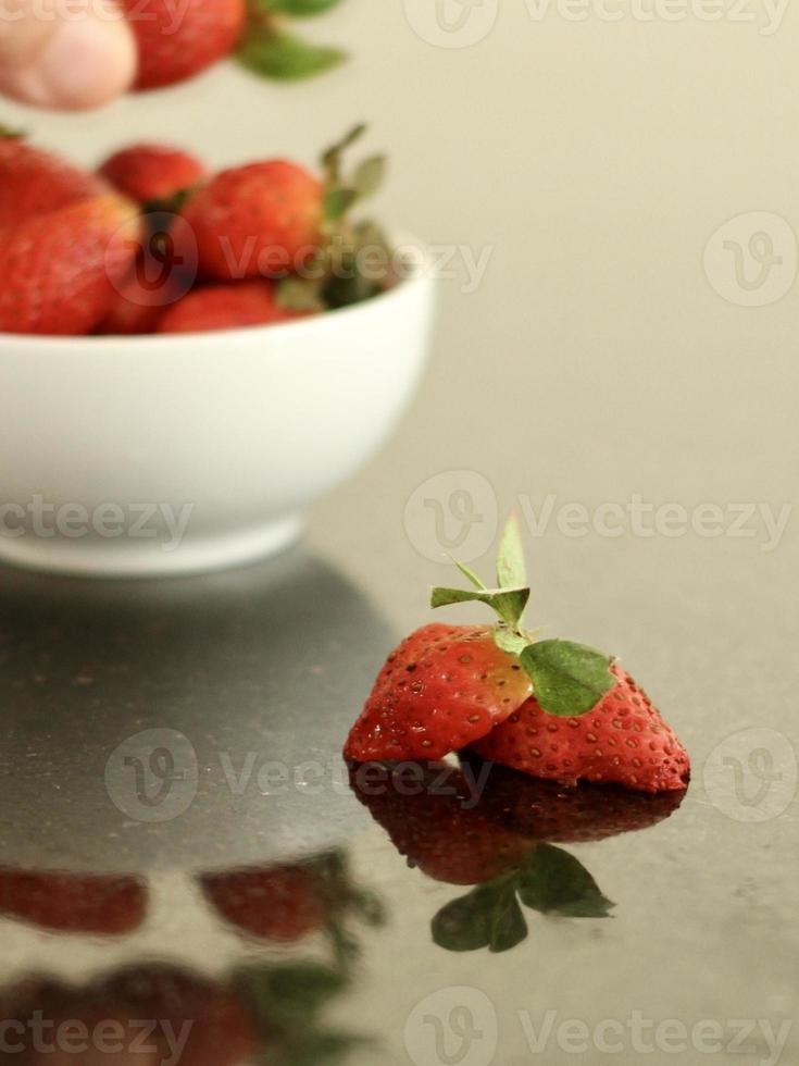 trancher la fraise sur une table de couleur inégale avec une main recadrée floue et une réflexion sur le dos. photo