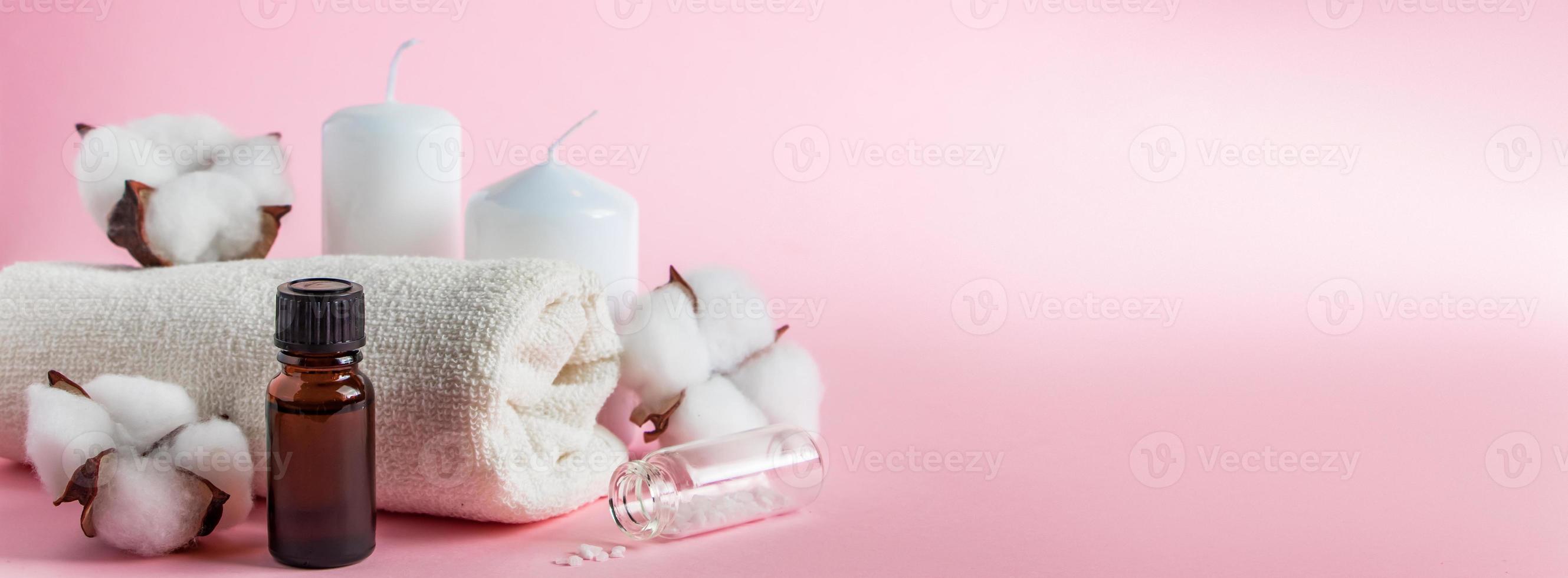 produits cosmétiques pour spa et aromathérapie. bougies, sel de mer, serviette et fleurs sur fond rose. concept de soins de la peau et de beauté. photo
