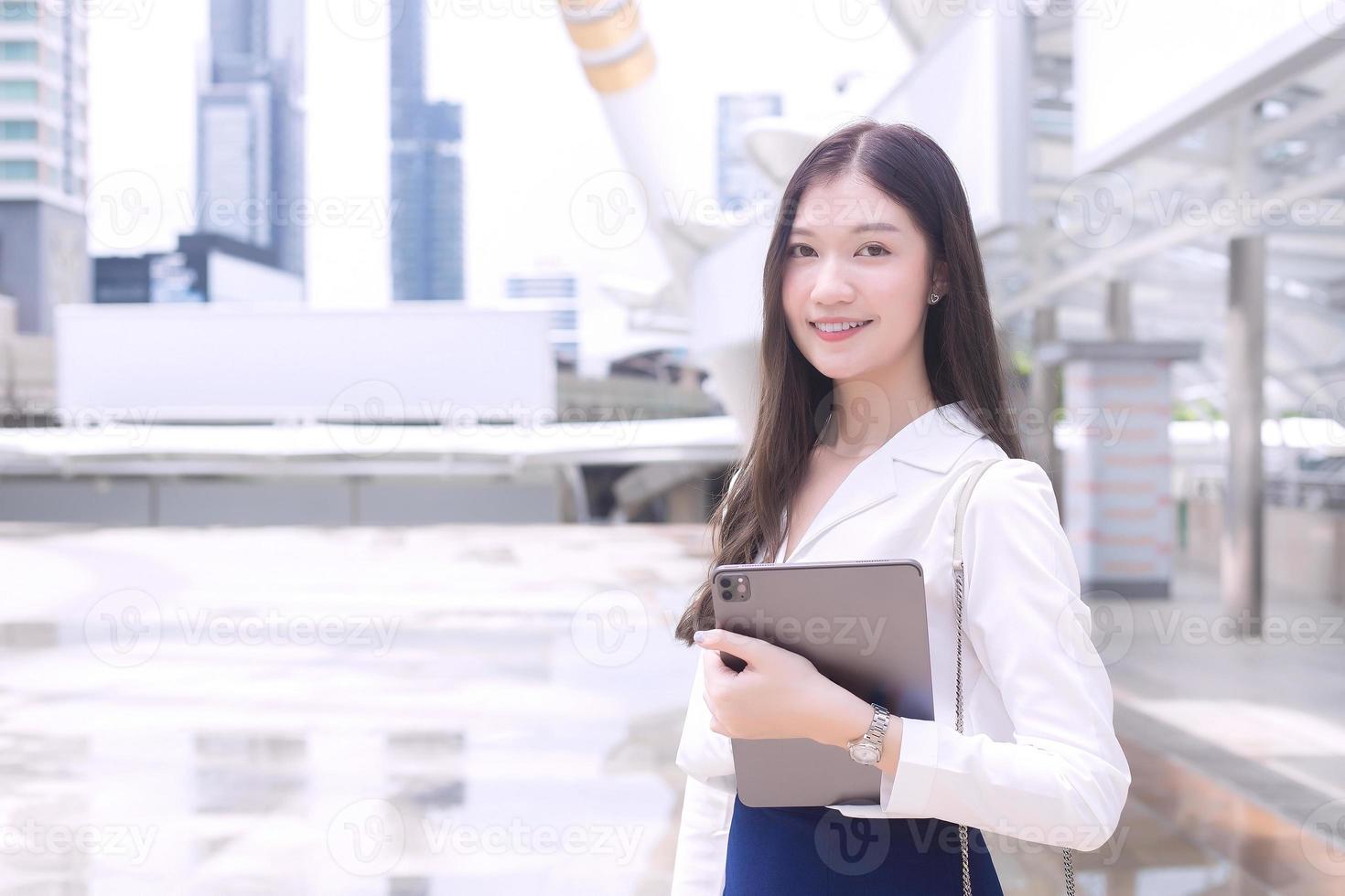 une jeune femme d'affaires asiatique se rend au bureau ou sur le lieu de travail qu'elle tient dans ses mains avec un bloc-notes sur le thème de l'arrière-plan des affaires. photo