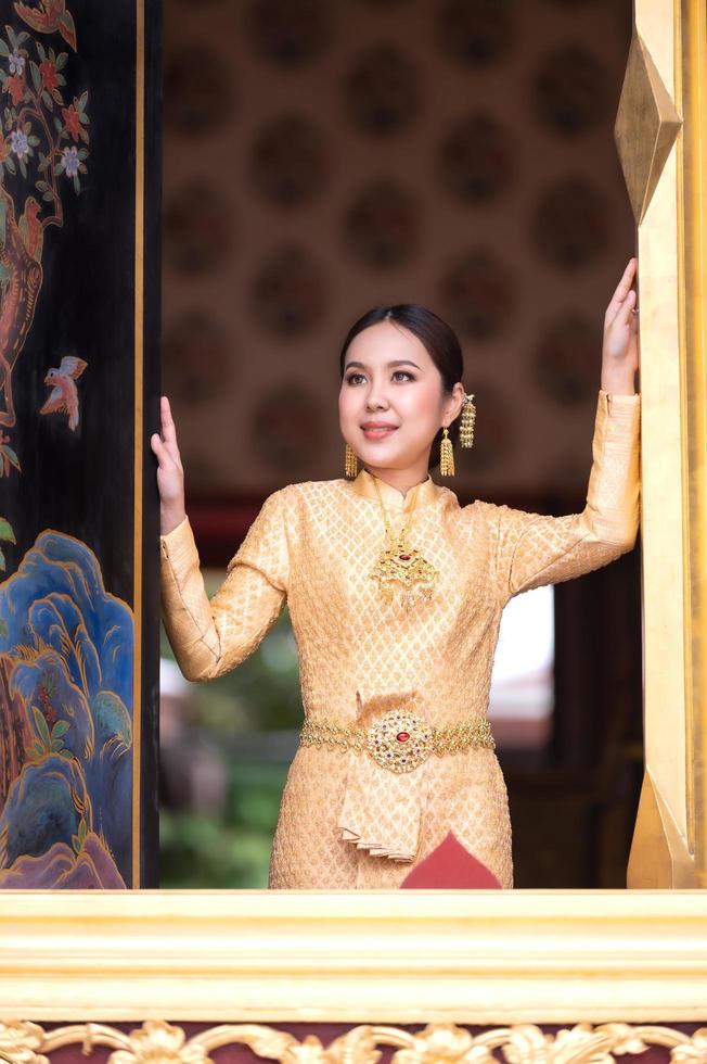 une belle et gracieuse femme thaïlandaise en robe thaïlandaise ornée de précieux bijoux se dresse dans un magnifique temple thaïlandais antique photo