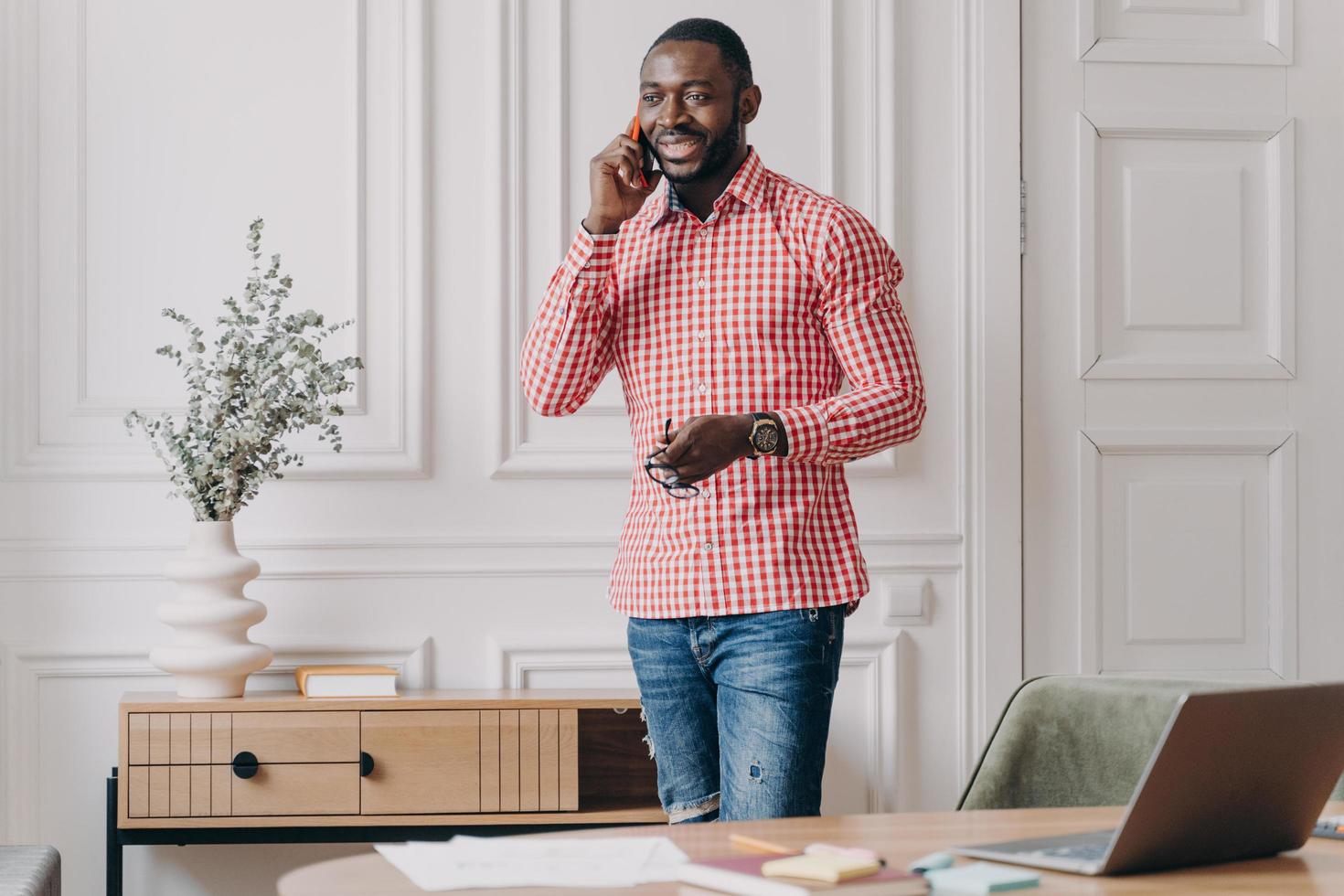 beau jeune homme d'affaires africain prospère dans des vêtements décontractés profitant d'un appel téléphonique, à l'aide d'un smartphone photo