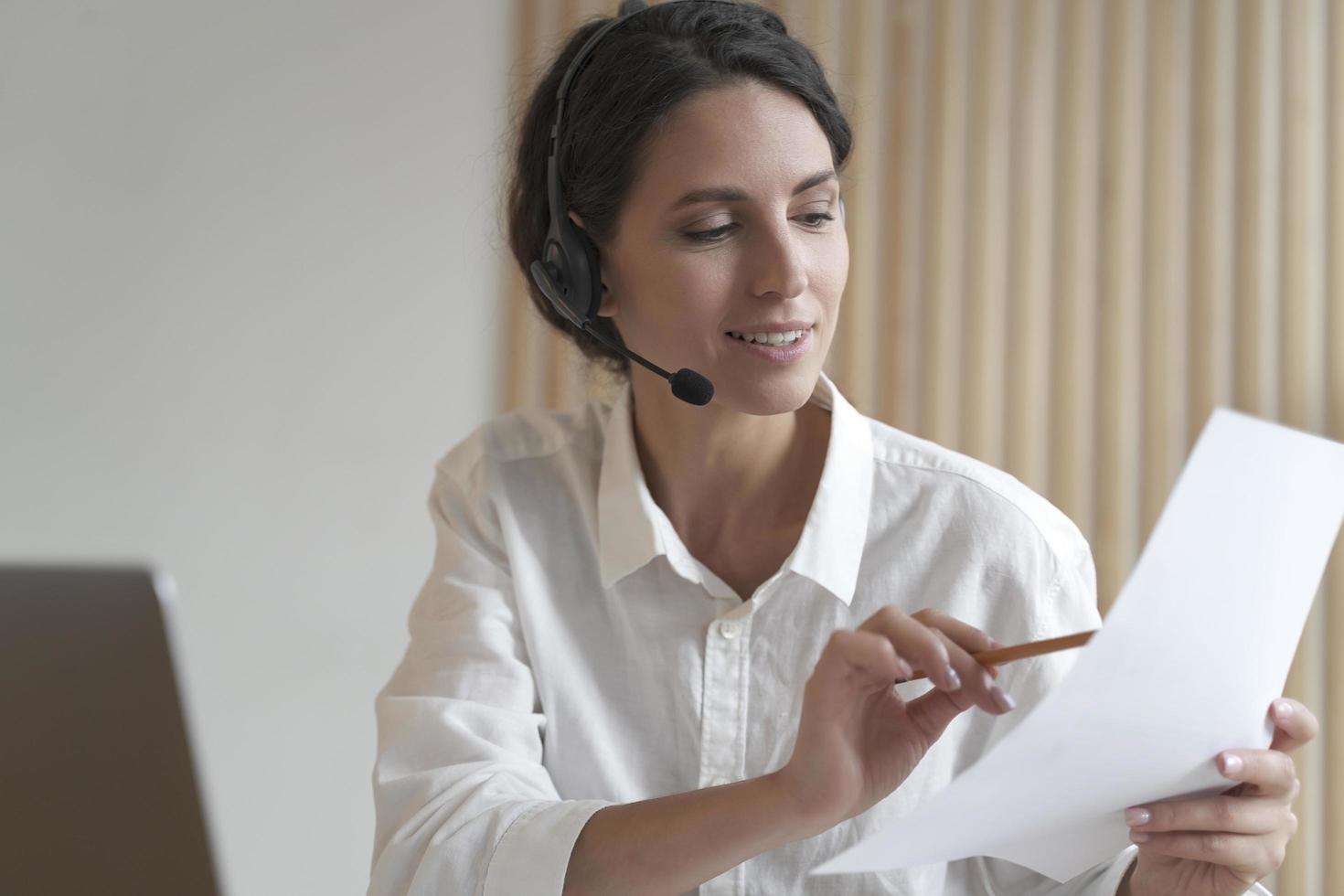 une femme d'affaires espagnole positive dans un casque est assise au bureau en ayant une vidéoconférence en ligne avec des partenaires photo