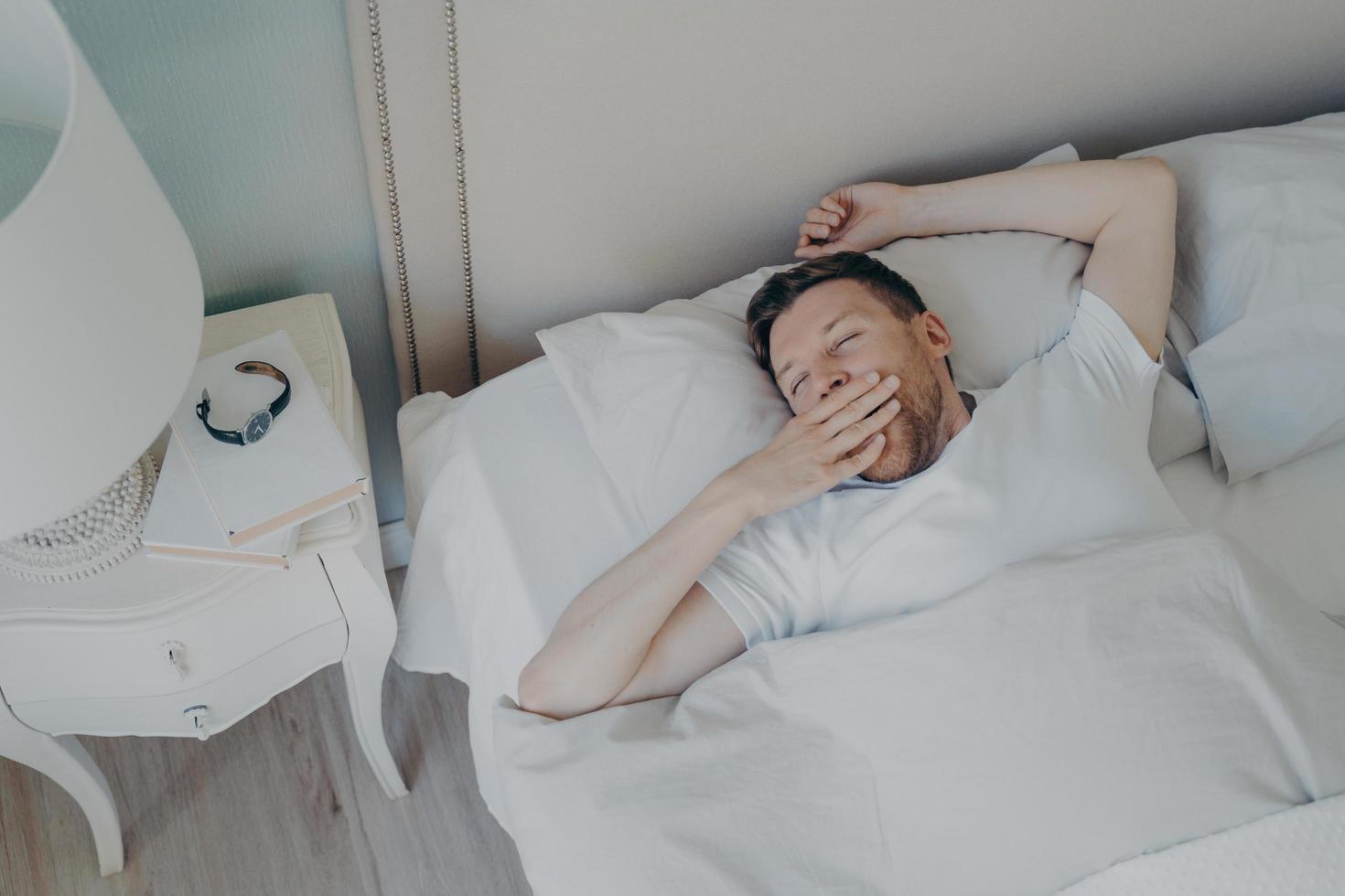 joyeux jeune homme séduisant se réveiller le matin au lit photo